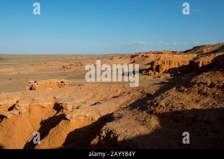 Die orangefarbenen Felsen von Bayan Zag, die im Allgemeinen als Flaming Cliffs in der Wüste Gobi, der Mongolei, bekannt sind und in denen wichtige Dinosaurier-Fossilien gefunden wurden. Stockfoto