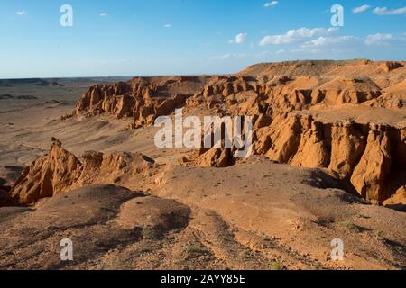 Die orangefarbenen Felsen von Bayan Zag, die im Allgemeinen als Flaming Cliffs in der Wüste Gobi, der Mongolei, bekannt sind und in denen wichtige Dinosaurier-Fossilien gefunden wurden. Stockfoto