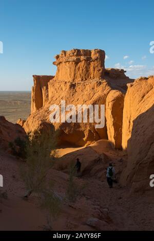 Touristen, die an den orangefarbenen Felsen von Bayan Zag, die im Allgemeinen als Flaming Cliffs in der Wüste Gobi, der Mongolei, bekannt sind, wo wichtige Dinosaurier-Fossil Stockfoto