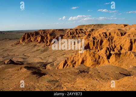 Die orangefarbenen Felsen von Bayan Zag, die im Allgemeinen als Flaming Cliffs in der Wüste Gobi, der Mongolei, bekannt sind und in denen wichtige Dinosaurier-Fossilien gefunden wurden. Stockfoto