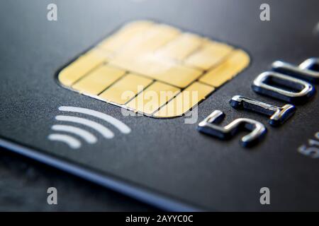 Nahaufnahme der schwarzen Plastikkreditkarte mit Chip und kontaktloser Zahlungstechnologie. Makrofotografie einer Bankkreditkarte auf einem Tisch. Draufsicht. Stockfoto