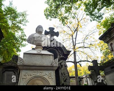 Alte Büste eines Mannes in weißem Stein an der Spitze eines monumentalen Grab von Grabkapellen und Kreuzen unter Herbstbäumen in einem Friedhof umgeben geschnitzt Stockfoto