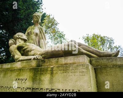 Trauerdenkmal aus weißem Stein mit den Statuen einer Frau trauernd ein starker Männer mit Bäumen im Hintergrund in einem monumentalen Friedhof Stockfoto