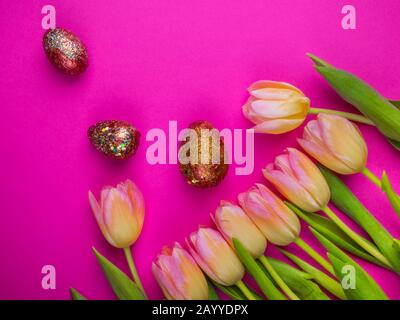 Mit Acrylfarbe bemalt, dekoriert mit glitzern ostereiern mit schönen Blumen - gelbe Tulpen auf pinkfarbenem Hintergrund, Kopierraum, Draufsicht Stockfoto