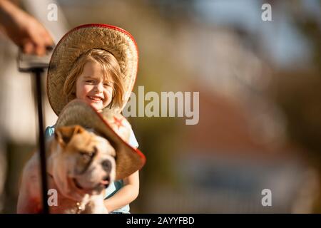 Mädchen und ihre Bulldogge, beide tragen Cowboyhüte, in einem roten Wagen gezogen. Stockfoto