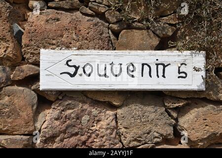 Handgefertigtes weißes Holzschild mit Souvenirs, die an der rustikalen Steinmauer befestigt sind. Pfeil nach links. In Betancuria, Fuerteventura eingenommen. Stockfoto