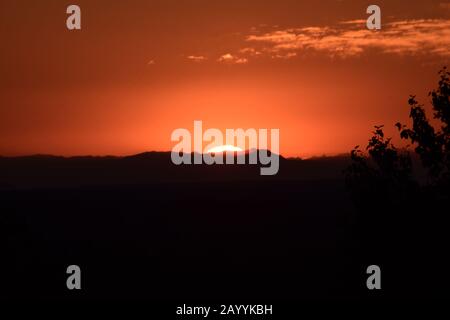 Helle Sonne, Die Über Dramatisch Silhouettierte Bergkette Gegen Orange Cloudy Sky Steigt Stockfoto