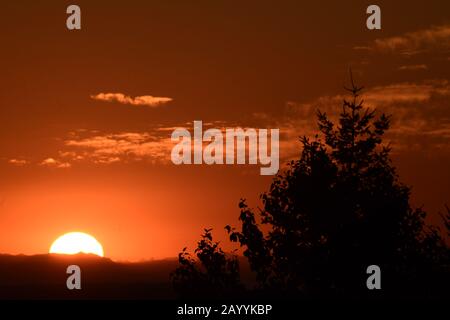 Helle Sonne, Die Über Dramatisch Silhouettierte Bergkette Gegen Orange Cloudy Sky Steigt Stockfoto