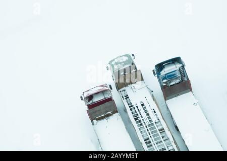 LKW unter dem Schnee. LKW nach Schneefall mit Schnee bedeckt. Lange LKWs stehen in einer Reihe Draufsicht. Transportkonzept. Schneebedeckte Fahrzeuge. Aeri Stockfoto