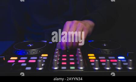 DJ spielt Musik ab. Sound Mixer Controller mit Knöpfen und Schiebereglern nah oben. Hände auf dem Mischdeck und Drehtische bei Dunkelheit mit beleuchteten Bedienelementen Stockfoto