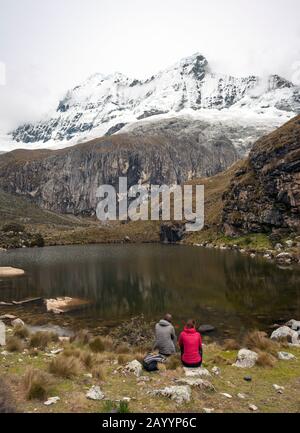 Ein Paar sitzt neben einem See auf der Wanderung der Laguna 69 in den Bergen der Cordillera Blanca im Norden Perus. Stockfoto