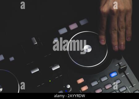 DJ spielt Musik ab. Sound Mixer Controller mit Knöpfen und Schiebereglern nah oben. Hände auf dem Mischdeck mit Drehtischen bei Dunkelheit mit beleuchteten Bedienelementen Stockfoto