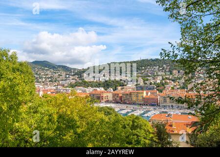 Blick durch die Bäume vom Burghügel des Alten Port Lympia mit farbenfrohen Gebäuden am Wasser und Booten im Yachthafen in Nizza, Frankreich. Stockfoto