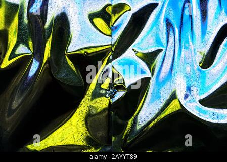 Hintergrund gelber und blauer Reflexionen auf Metallblechen. Die Form der Reflexionen ist sprunghaft, das Gesamtbild ist bunt kühl. Stockfoto