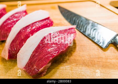 Wunderschönes Foto von Picanha (obere Sirloinkappe) schneidet auf einem Holzschneidbrett und einem schönen, maßgeschneiderten Stahlmesser aus Damast mit Arkasas-Brise-Muster. Stockfoto