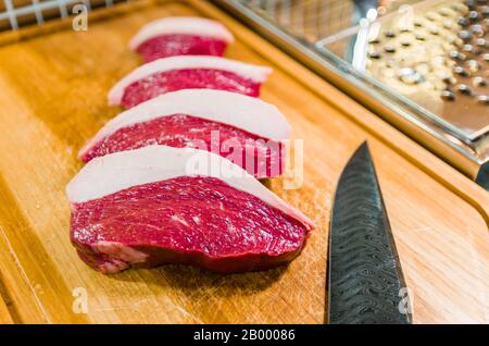 Wunderschönes Foto von Picanha (obere Sirloinkappe) schneidet auf einem Holzschneidbrett und einem schönen, maßgeschneiderten Stahlmesser aus Damast mit Arkasas-Brise-Muster. Stockfoto