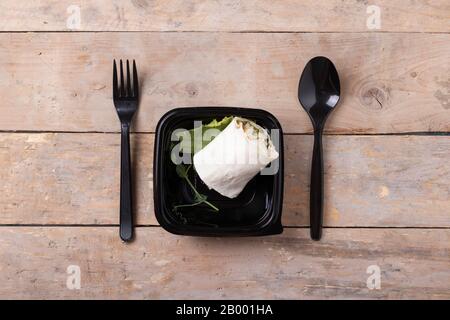 Leckeres, frisches Wickel-Sandwich mit Huhn und Gemüse in schwarzer Schachtel auf Holztisch, Draufsicht Stockfoto