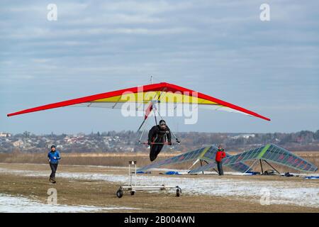 2020-02-09 Byshiv, Ukraine. Drachenflieger starten auf dem Flugplatz. Ein leuchtendes Hängegleiter in der Luft andere Piloten sind startbereit Stockfoto