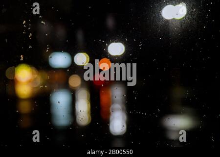 In der Regenzeit fällt in der Nacht Regen auf dem Autofenster mit leichtem Bokeh Stockfoto