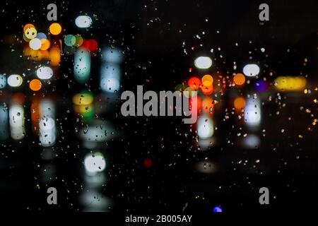 In der Regenzeit fällt Regen auf dem Fenster mit der Stadt mit leichtem Straßenlicht Stockfoto