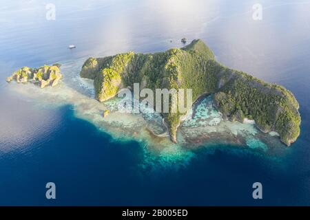 Zerklüftete Kalksteininseln ragen aus der heiteren Seescape in Raja Ampat, Indonesien auf. Diese tropische Region wird als Herz des Korallendreiecks bezeichnet. Stockfoto