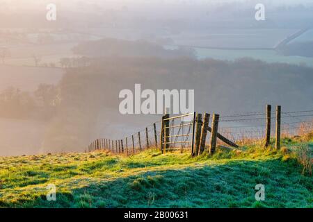 Zaun und Bauerntor Martinsell Hill an einem nebligen Wintermorgen bei Sonnenaufgang. In der Nähe von Oare, Vale of Pewsey, Wiltshire, England Stockfoto