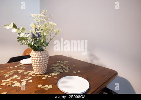 Vase mit einem Blumenstrauß aus weißen und blauen Blumen auf einem Holztisch vor grauem Hintergrund. Goldenes Konfetti auf dem Tisch. Stockfoto