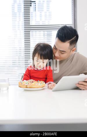 Der junge Vater und seine Tochter essen Pizza und benutzen das ipad. Stockfoto