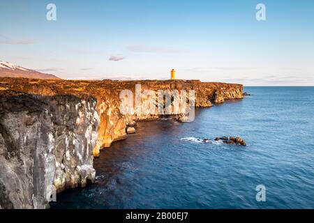 Der orangefarbene Leuchtturm von Oendverdarnes steht auf Klippen, lavastischer Küste, Oendveroarnes, Snaefellsjoekull National Park, Snaefellsnes Peninsula Stockfoto