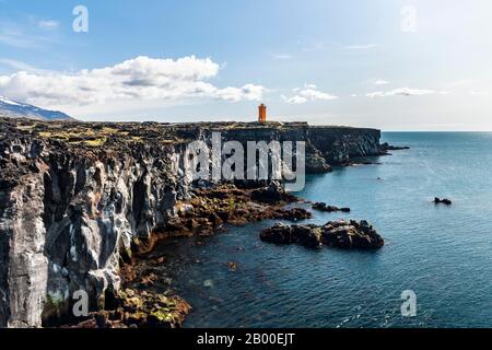 Der orangefarbene Leuchtturm von Oendverdarnes steht auf Klippen, lavastischer Küste, Oendveroarnes, Snaefellsjoekull National Park, Snaefellsnes Peninsula Stockfoto