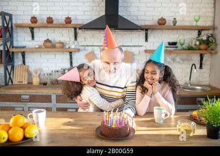 Zwei dunkelhäutige Mädchen feiern Geburtstag mit ihrem Opa Stockfoto