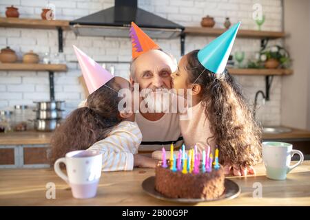 Dunkelhäutige Mädchen feiern seinen Großdamen bithday und küssen ihn auf Wangen Stockfoto