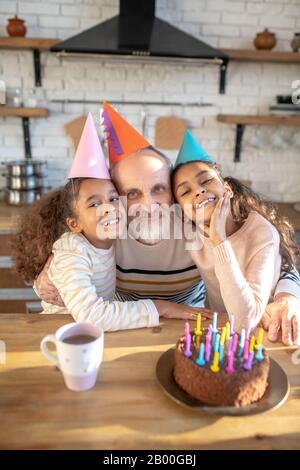 Bärtiger grauhaariger Mann und seine dunkelhäutigen Mädchen feiern den Bithday Stockfoto
