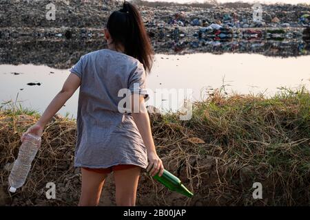 Die Rückenfrau steht in der Hand, hat eine grüne Glasflasche und eine durchsichtige Plastikflasche auf dem großen Müllgrund in den Bergen, Diese Abfälle stammen aus Urban und ich Stockfoto