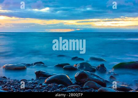 Sonnenuntergang über dem Meer und große Steine am Kieselstrand - Sonnenuntergang mit Wasser in Bewegungsunschärfe Stockfoto