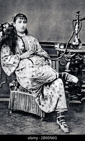 Algerien: Arabische Frau mit Shisha-Pfeife, 1880er. Eine Wasserpfeife (Hindustani: Huqqah), auch Wasserpfeife genannt, ist ein ein- oder mehrstämmigiger (oft glasbasierter) Rauchmelder, bei dem der Rauch durch Wasser gekühlt und gefiltert wird. Der gerauchte Tabak wird im Vereinigten Königreich, den Vereinigten Staaten und Kanada als Narghile oder Shisha (Sheesha) bezeichnet. Stockfoto