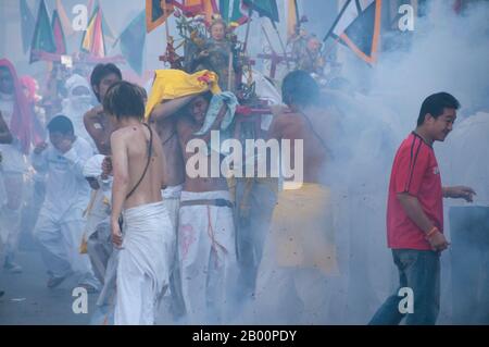 Thailand: Schreinträger Rennen durch die Straßen, um explodierende Feuerwerkskörper und den ohrenbetäubenden Lärm zu vermeiden, Phuket Vegetarian Festival. Das Vegetarische Festival ist ein religiöses Festival, das jährlich auf der Insel Phuket im Süden Thailands stattfindet. Es zieht Massen von Zuschauern wegen vieler der ungewöhnlichen religiösen Rituale an, die durchgeführt werden. Viele religiöse Anhänger werden sich mit Schwertern niederschlagen, ihre Wangen mit scharfen Gegenständen durchbohren und andere schmerzhafte Handlungen begehen. Stockfoto
