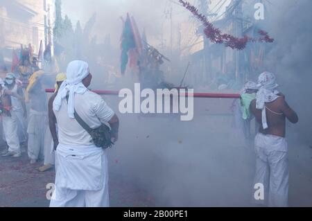 Thailand: Ohrenbetäubende Feuerwerkskörper explodieren über den Köpfen der Schreinträger, während sie durch die Straßen Rennen, Phuket Vegetarian Festival. Das Vegetarische Festival ist ein religiöses Festival, das jährlich auf der Insel Phuket im Süden Thailands stattfindet. Es zieht Massen von Zuschauern wegen vieler der ungewöhnlichen religiösen Rituale an, die durchgeführt werden. Viele religiöse Anhänger werden sich mit Schwertern niederschlagen, ihre Wangen mit scharfen Gegenständen durchbohren und andere schmerzhafte Handlungen begehen. Stockfoto