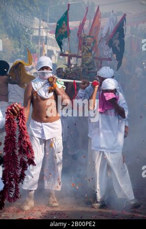 Thailand: Ohrenbetäubende Feuerwerkskörper explodieren über den Köpfen der Schreinträger, während sie durch die Straßen Rennen, Phuket Vegetarian Festival. Das Vegetarische Festival ist ein religiöses Festival, das jährlich auf der Insel Phuket im Süden Thailands stattfindet. Es zieht Massen von Zuschauern wegen vieler der ungewöhnlichen religiösen Rituale an, die durchgeführt werden. Viele religiöse Anhänger werden sich mit Schwertern niederschlagen, ihre Wangen mit scharfen Gegenständen durchbohren und andere schmerzhafte Handlungen begehen. Stockfoto