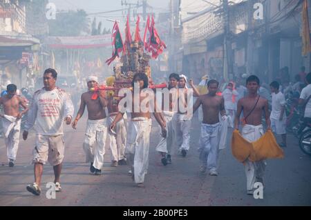 Thailand: Schreinträger Rennen durch die Straßen, um explodierende Feuerwerkskörper und den ohrenbetäubenden Lärm zu vermeiden, Phuket Vegetarian Festival. Das Vegetarische Festival ist ein religiöses Festival, das jährlich auf der Insel Phuket im Süden Thailands stattfindet. Es zieht Massen von Zuschauern wegen vieler der ungewöhnlichen religiösen Rituale an, die durchgeführt werden. Viele religiöse Anhänger werden sich mit Schwertern niederschlagen, ihre Wangen mit scharfen Gegenständen durchbohren und andere schmerzhafte Handlungen begehen. Stockfoto