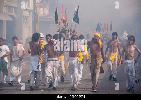 Thailand: Schreinträger Rennen durch die Straßen, um explodierende Feuerwerkskörper und den ohrenbetäubenden Lärm zu vermeiden, Phuket Vegetarian Festival. Das Vegetarische Festival ist ein religiöses Festival, das jährlich auf der Insel Phuket im Süden Thailands stattfindet. Es zieht Massen von Zuschauern wegen vieler der ungewöhnlichen religiösen Rituale an, die durchgeführt werden. Viele religiöse Anhänger werden sich mit Schwertern niederschlagen, ihre Wangen mit scharfen Gegenständen durchbohren und andere schmerzhafte Handlungen begehen. Stockfoto