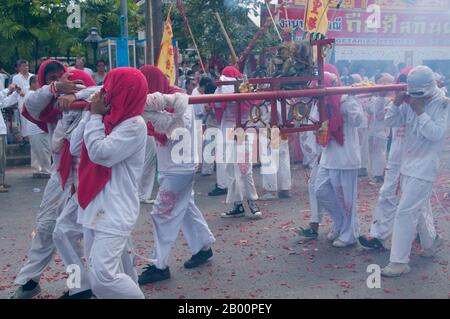 Thailand: Schreinträger Rennen durch die Straßen, um explodierende Feuerwerkskörper und den ohrenbetäubenden Lärm zu vermeiden, Phuket Vegetarian Festival. Das Vegetarische Festival ist ein religiöses Festival, das jährlich auf der Insel Phuket im Süden Thailands stattfindet. Es zieht Massen von Zuschauern wegen vieler der ungewöhnlichen religiösen Rituale an, die durchgeführt werden. Viele religiöse Anhänger werden sich mit Schwertern niederschlagen, ihre Wangen mit scharfen Gegenständen durchbohren und andere schmerzhafte Handlungen begehen. Stockfoto