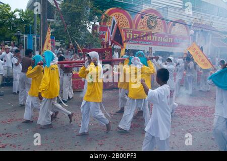 Thailand: Schreinträger Rennen durch die Straßen, um explodierende Feuerwerkskörper und den ohrenbetäubenden Lärm zu vermeiden, Phuket Vegetarian Festival. Das Vegetarische Festival ist ein religiöses Festival, das jährlich auf der Insel Phuket im Süden Thailands stattfindet. Es zieht Massen von Zuschauern wegen vieler der ungewöhnlichen religiösen Rituale an, die durchgeführt werden. Viele religiöse Anhänger werden sich mit Schwertern niederschlagen, ihre Wangen mit scharfen Gegenständen durchbohren und andere schmerzhafte Handlungen begehen. Stockfoto