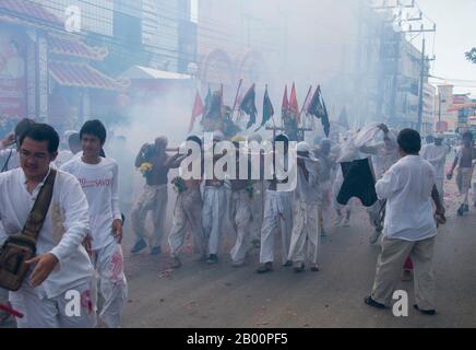 Thailand: Schreinträger Rennen durch die Straßen, um explodierende Feuerwerkskörper und den ohrenbetäubenden Lärm zu vermeiden, Phuket Vegetarian Festival. Das Vegetarische Festival ist ein religiöses Festival, das jährlich auf der Insel Phuket im Süden Thailands stattfindet. Es zieht Massen von Zuschauern wegen vieler der ungewöhnlichen religiösen Rituale an, die durchgeführt werden. Viele religiöse Anhänger werden sich mit Schwertern niederschlagen, ihre Wangen mit scharfen Gegenständen durchbohren und andere schmerzhafte Handlungen begehen. Stockfoto