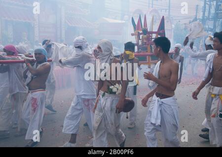 Thailand: Schreinträger Rennen durch die Straßen, um explodierende Feuerwerkskörper und den ohrenbetäubenden Lärm zu vermeiden, Phuket Vegetarian Festival. Das Vegetarische Festival ist ein religiöses Festival, das jährlich auf der Insel Phuket im Süden Thailands stattfindet. Es zieht Massen von Zuschauern wegen vieler der ungewöhnlichen religiösen Rituale an, die durchgeführt werden. Viele religiöse Anhänger werden sich mit Schwertern niederschlagen, ihre Wangen mit scharfen Gegenständen durchbohren und andere schmerzhafte Handlungen begehen. Stockfoto