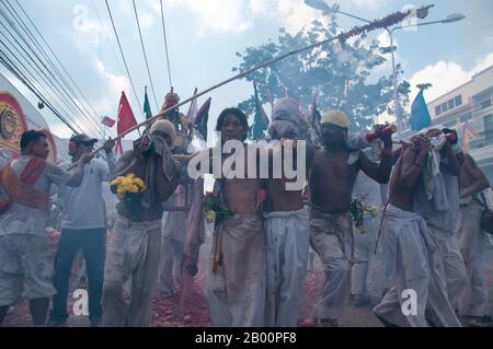 Thailand: Schreinträger Rennen durch die Straßen, um explodierende Feuerwerkskörper und den ohrenbetäubenden Lärm zu vermeiden, Phuket Vegetarian Festival. Das Vegetarische Festival ist ein religiöses Festival, das jährlich auf der Insel Phuket im Süden Thailands stattfindet. Es zieht Massen von Zuschauern wegen vieler der ungewöhnlichen religiösen Rituale an, die durchgeführt werden. Viele religiöse Anhänger werden sich mit Schwertern niederschlagen, ihre Wangen mit scharfen Gegenständen durchbohren und andere schmerzhafte Handlungen begehen. Stockfoto