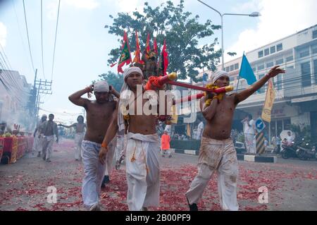Thailand: Schreinträger Rennen durch die Straßen, um explodierende Feuerwerkskörper und den ohrenbetäubenden Lärm zu vermeiden, Phuket Vegetarian Festival. Das Vegetarische Festival ist ein religiöses Festival, das jährlich auf der Insel Phuket im Süden Thailands stattfindet. Es zieht Massen von Zuschauern wegen vieler der ungewöhnlichen religiösen Rituale an, die durchgeführt werden. Viele religiöse Anhänger werden sich mit Schwertern niederschlagen, ihre Wangen mit scharfen Gegenständen durchbohren und andere schmerzhafte Handlungen begehen. Stockfoto