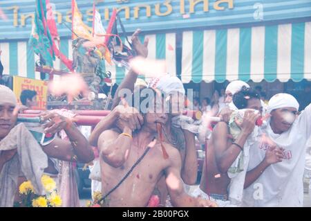 Thailand: Schreinträger Rennen durch die Straßen, um explodierende Feuerwerkskörper und den ohrenbetäubenden Lärm zu vermeiden, Phuket Vegetarian Festival. Das Vegetarische Festival ist ein religiöses Festival, das jährlich auf der Insel Phuket im Süden Thailands stattfindet. Es zieht Massen von Zuschauern wegen vieler der ungewöhnlichen religiösen Rituale an, die durchgeführt werden. Viele religiöse Anhänger werden sich mit Schwertern niederschlagen, ihre Wangen mit scharfen Gegenständen durchbohren und andere schmerzhafte Handlungen begehen. Stockfoto