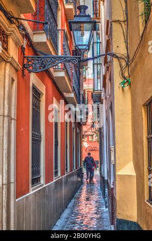 Enge Straße im Barrio Santa Cruz mit Menschen zu Fuß. Nasses Pflaster. Typische Farben in den Gebäuden. Stockfoto