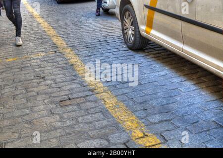 Kopfsteinpflaster mit gelber Linie. Fußgänger und Fahrzeuge. Sevilla, Spanien. Stockfoto
